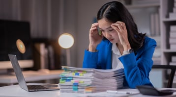 Lady with headache staring at a pile of paper documents